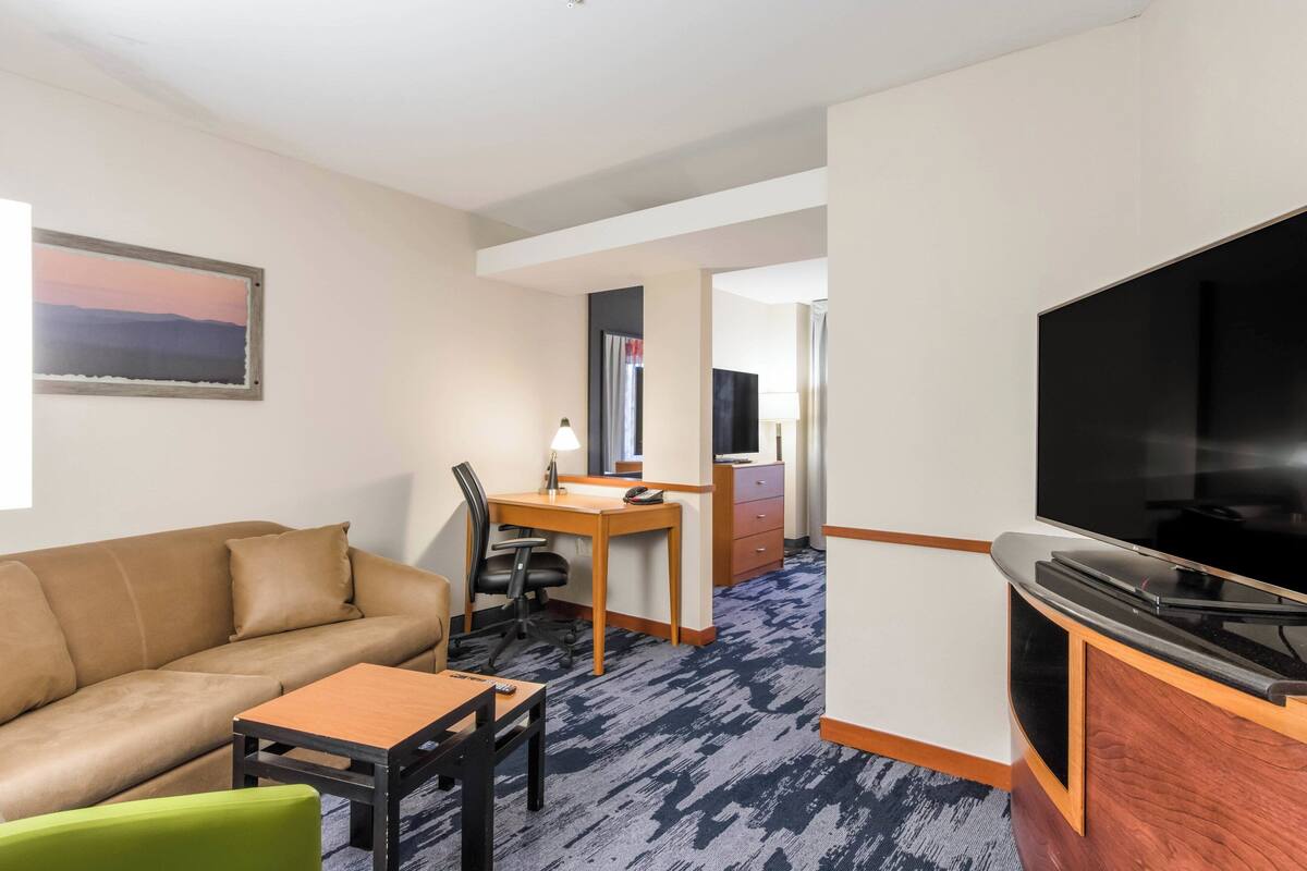 Habitación de hotel con sofá, escritorio y silla, televisor y piso alfombrado.