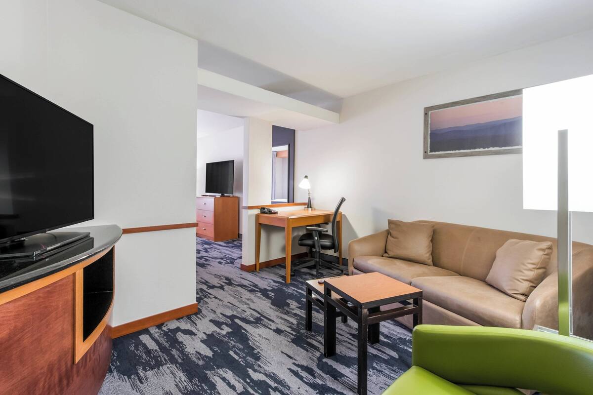 Habitación de hotel con televisión, escritorio con lámpara, sofá y un cuadro en la pared.