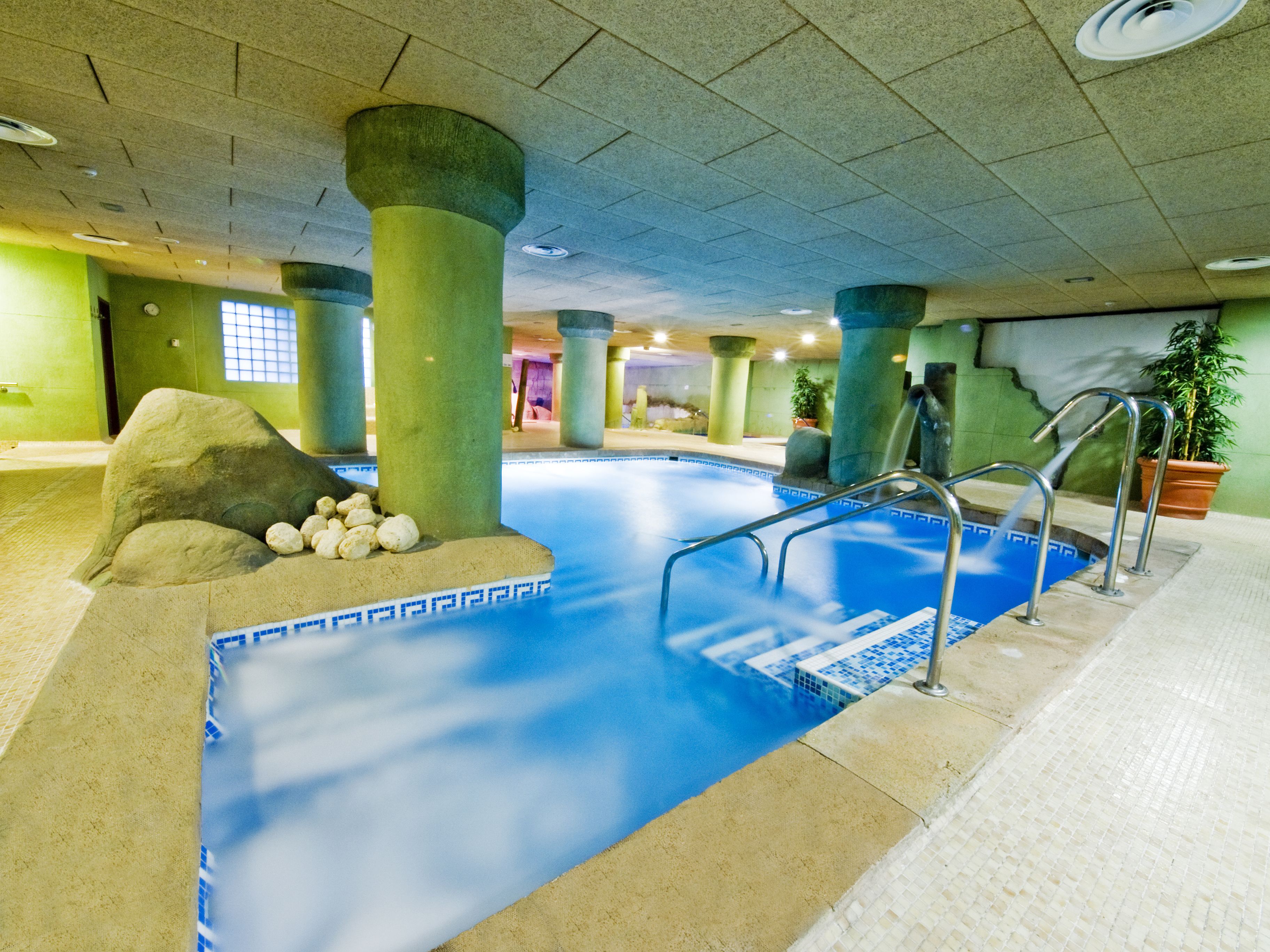 An indoor swimming pool with clear blue water, surrounded by columns and a tiled floor.