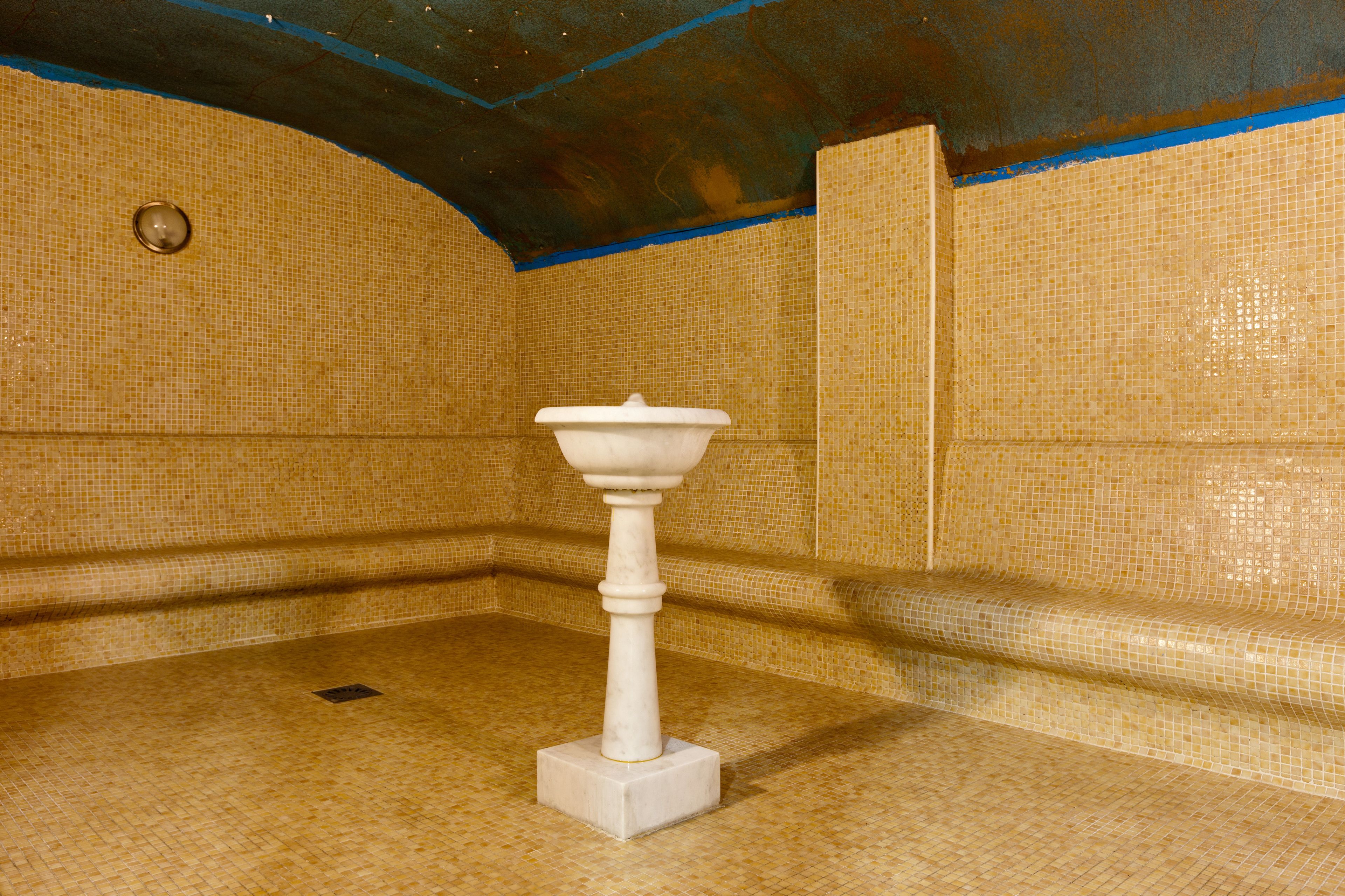 Un baño con lavamanos pedestal blanco, paredes con azulejos y desagüe en el suelo.