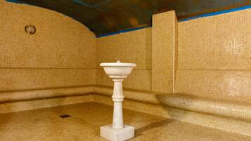 Un baño con lavamanos pedestal blanco, paredes con azulejos y desagüe en el suelo.