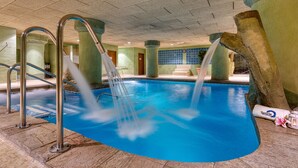 Una piscina interior con agua cristalina, escaleras metálicas y suelo de piedra.