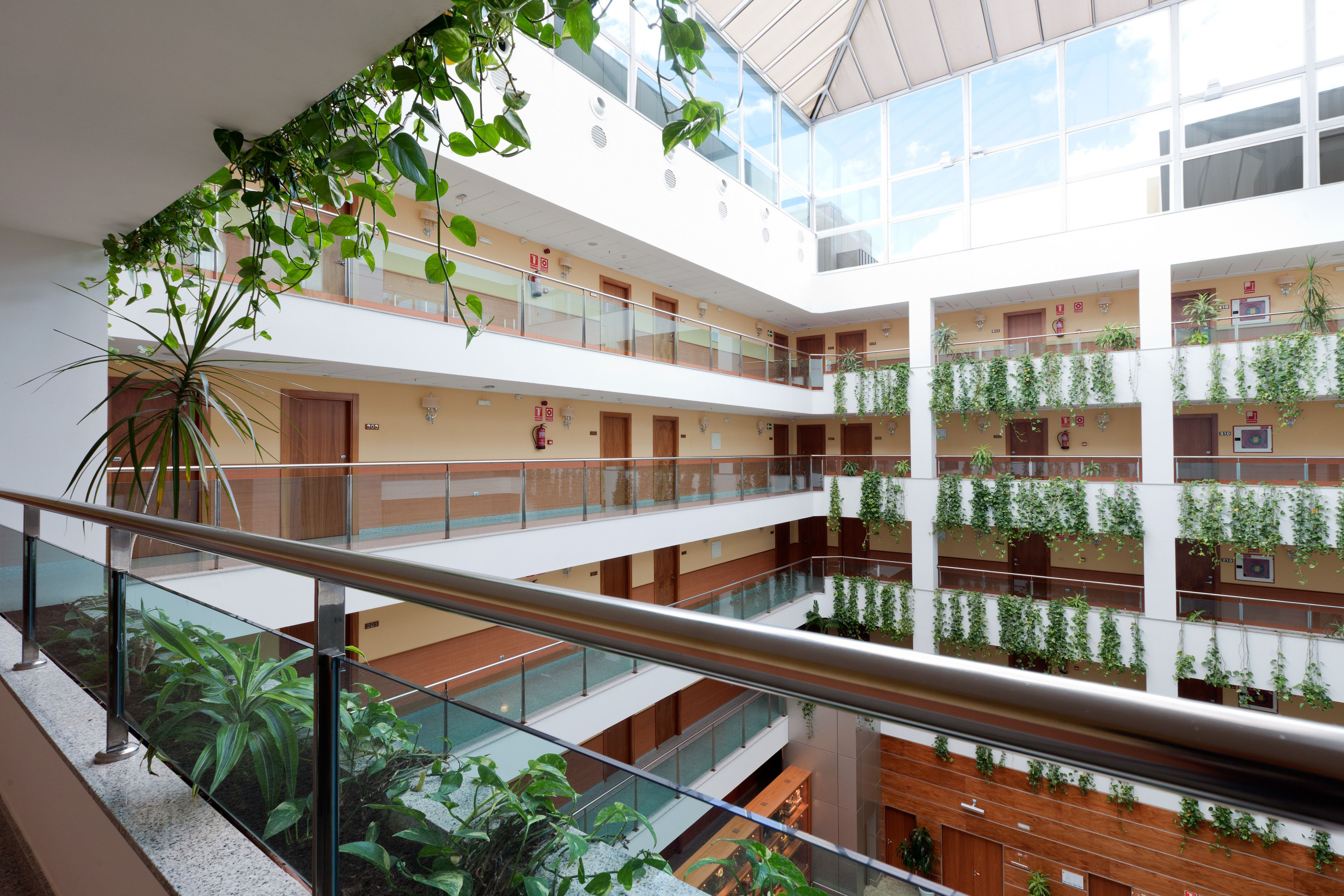 Un atrio de varios niveles con barandas de vidrio, plantas de interior y un diseño arquitectónico moderno.