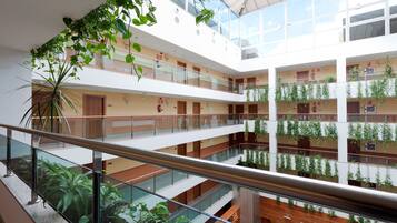 Un atrio de varios niveles con barandas de vidrio, plantas de interior y un diseño arquitectónico moderno.
