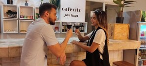 Een café met een toonbank, planken met spullen, en een bord waarop staat 'cafecito por favor'.