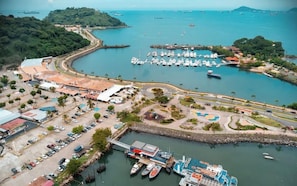 Marina costera con barcos, zona de estacionamiento y edificios, junto a una carretera curva.