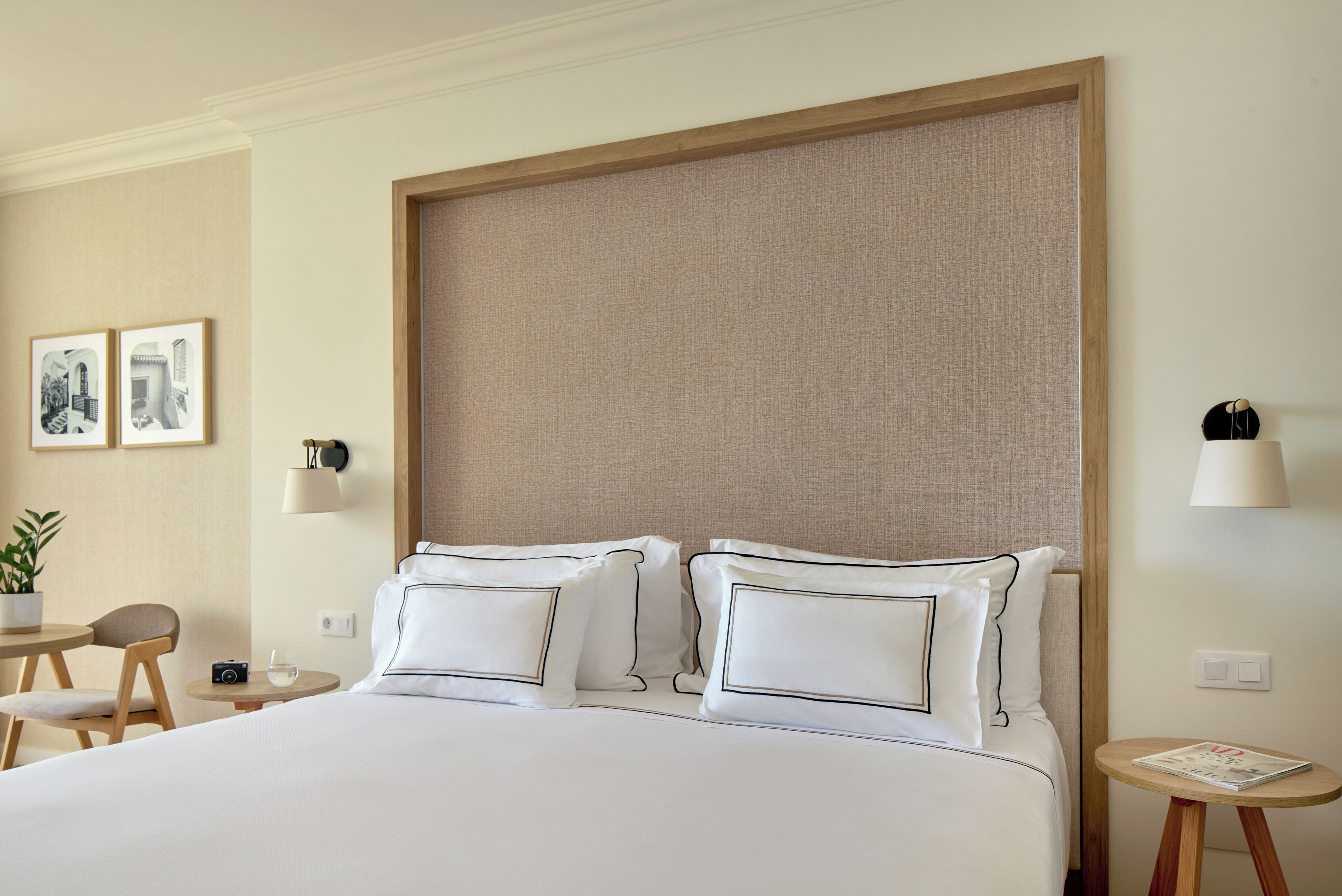 A hotel room with a large bed, two bedside tables, a chair, a small table with a camera, and framed pictures on the wall.