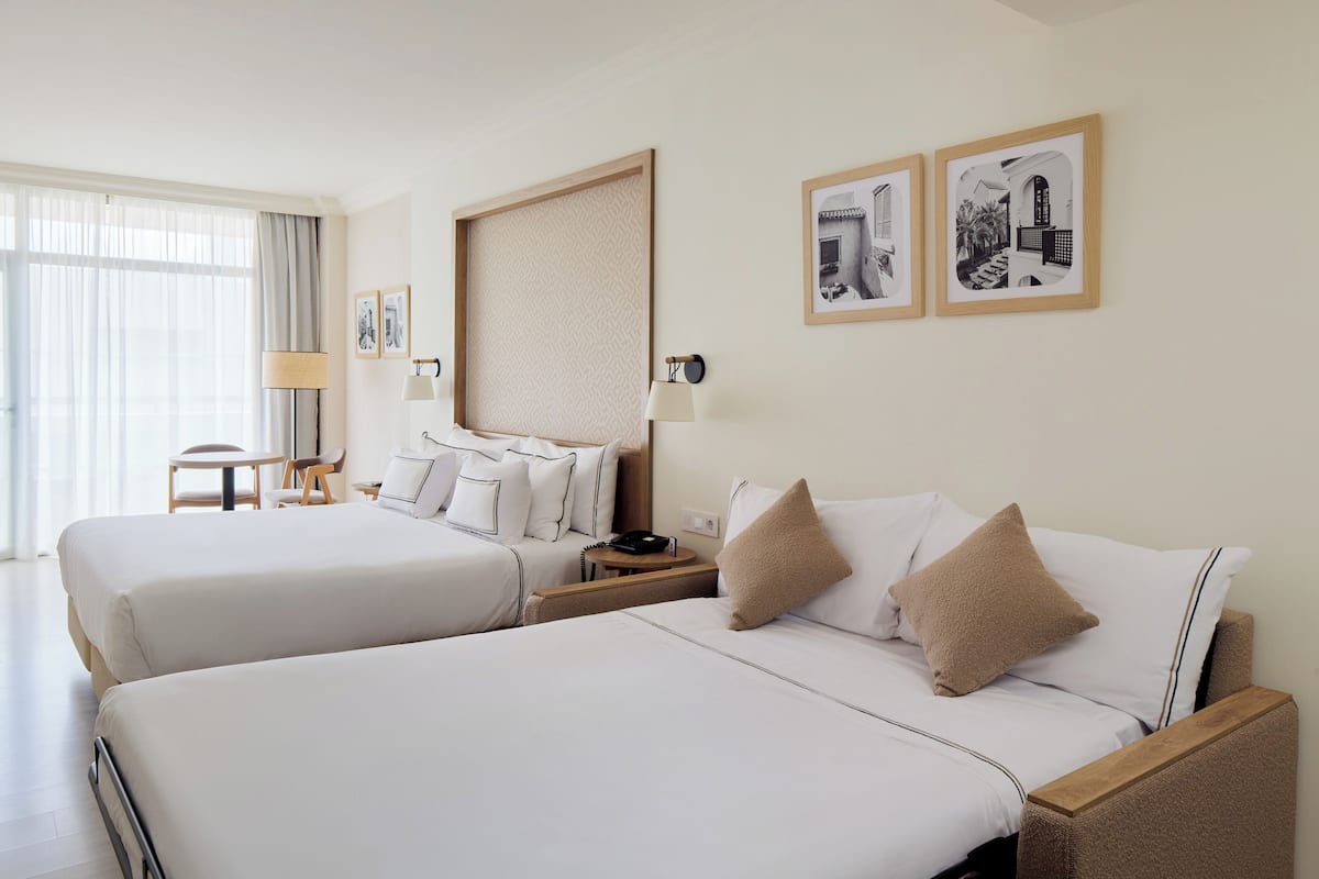 Hotellihuone, jossa on kaksi sänkyä, työpöytä, tuoli ja suuri ikkuna.