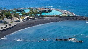 A coastal resort with a beach, a pool area, and a rocky shoreline. - Meliá Costa Atlantis Tenerife (Puerto de la Cruz)