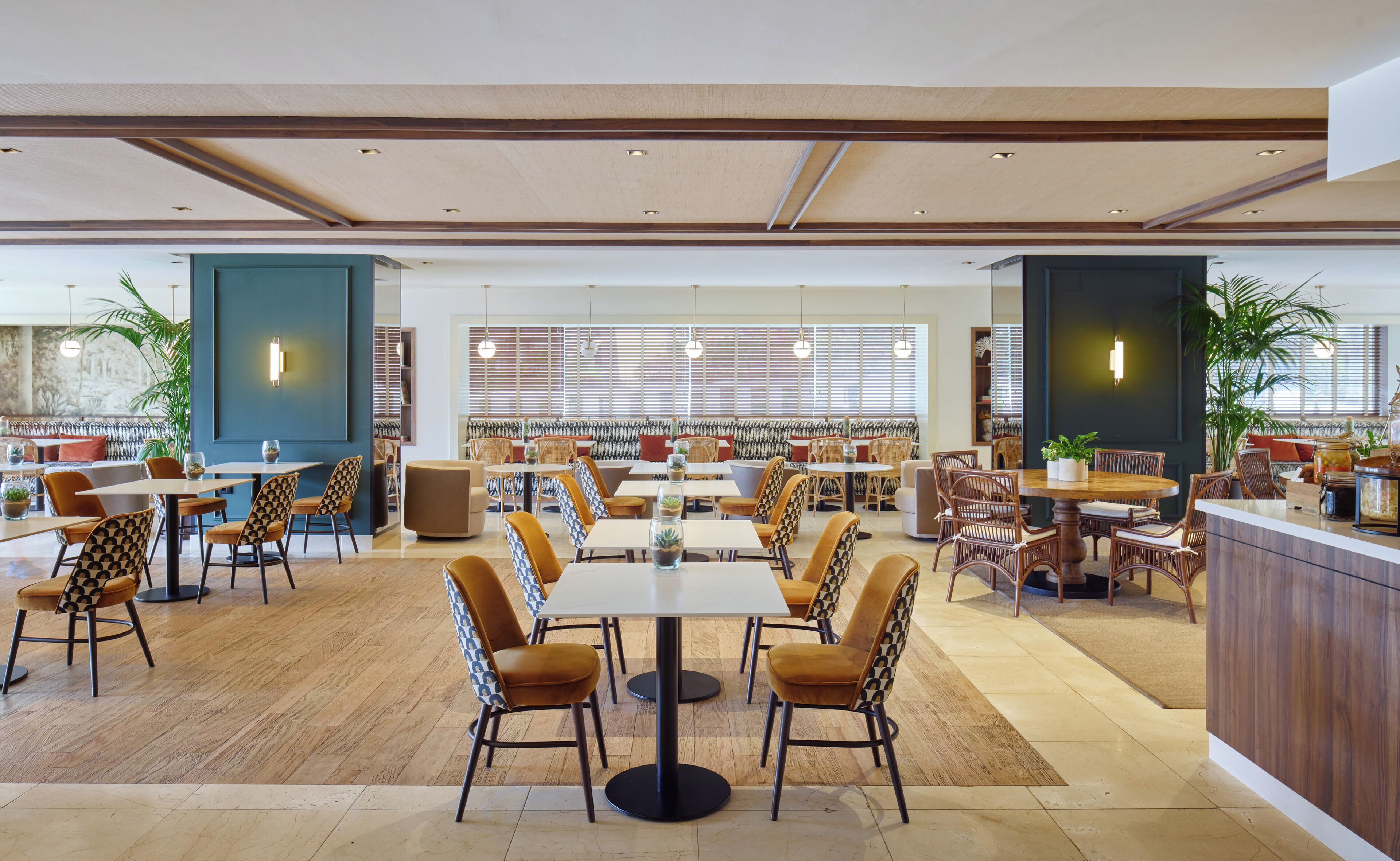 Un restaurante espacioso con varias zonas de comedor, pisos de madera y grandes ventanales con persianas.