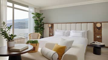 Habitación de hotel con una cama grande, vistas al exterior, una silla, una mesa y una planta en maceta.