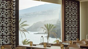 A restaurant with tables set for dining, a view of the ocean, and decorative panels. - Meliá Costa Atlantis Tenerife (Puerto de la Cruz)