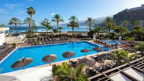 A pool area with lounge chairs and umbrellas, overlooking a beach and ocean. - Meliá Costa Atlantis Tenerife (Puerto de la Cruz)