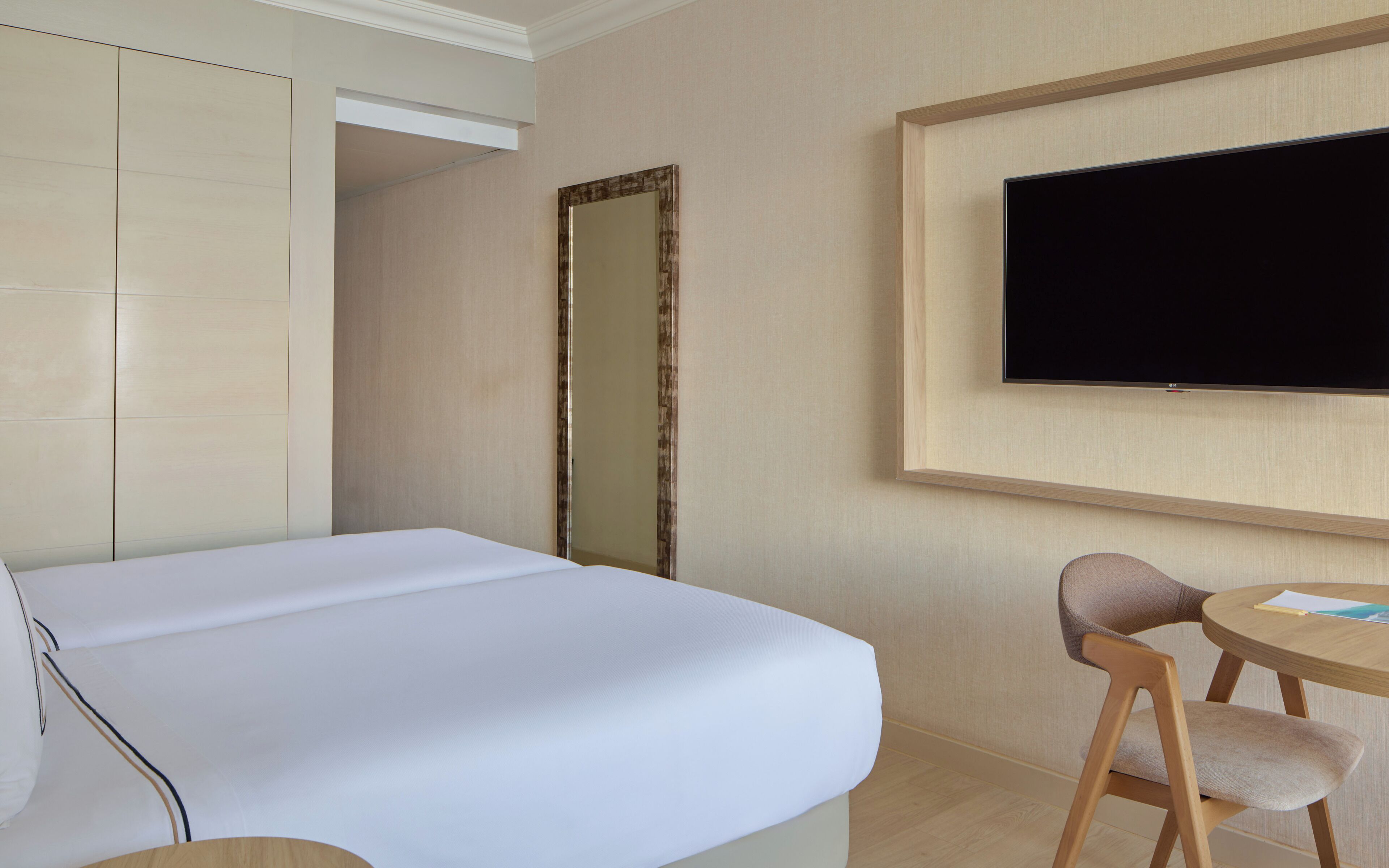 Una habitación de hotel con una cama, un televisor montado en la pared, una silla y una mesita.