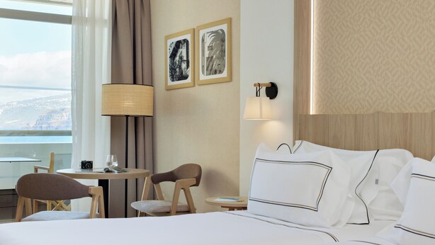 A hotel room with a bed, a desk with a chair, a lamp, and two framed pictures on the wall.