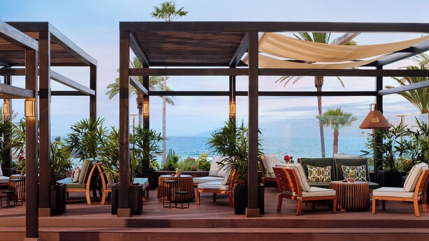 An outdoor seating area with wooden furniture, a canopy, and a view of the ocean. - Meliá Costa Atlantis Tenerife (Puerto de la Cruz)