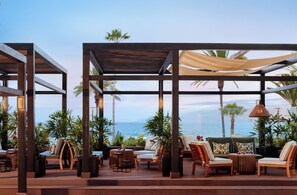 An outdoor seating area with wooden furniture, a canopy, and a view of the ocean. - Meliá Costa Atlantis Tenerife (Puerto de la Cruz)