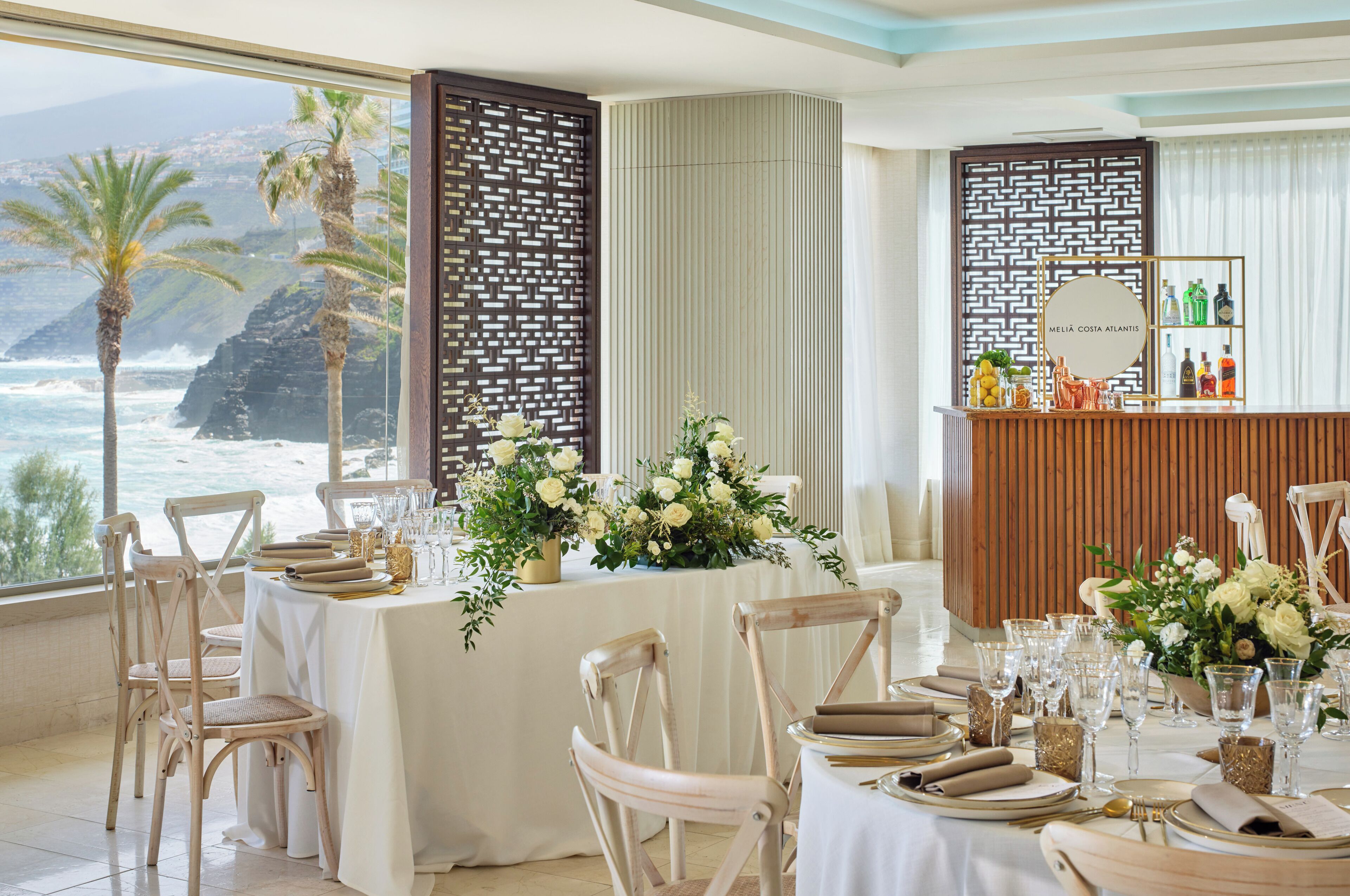 Comedor con vista al océano, manteles blancos y sillas de madera.