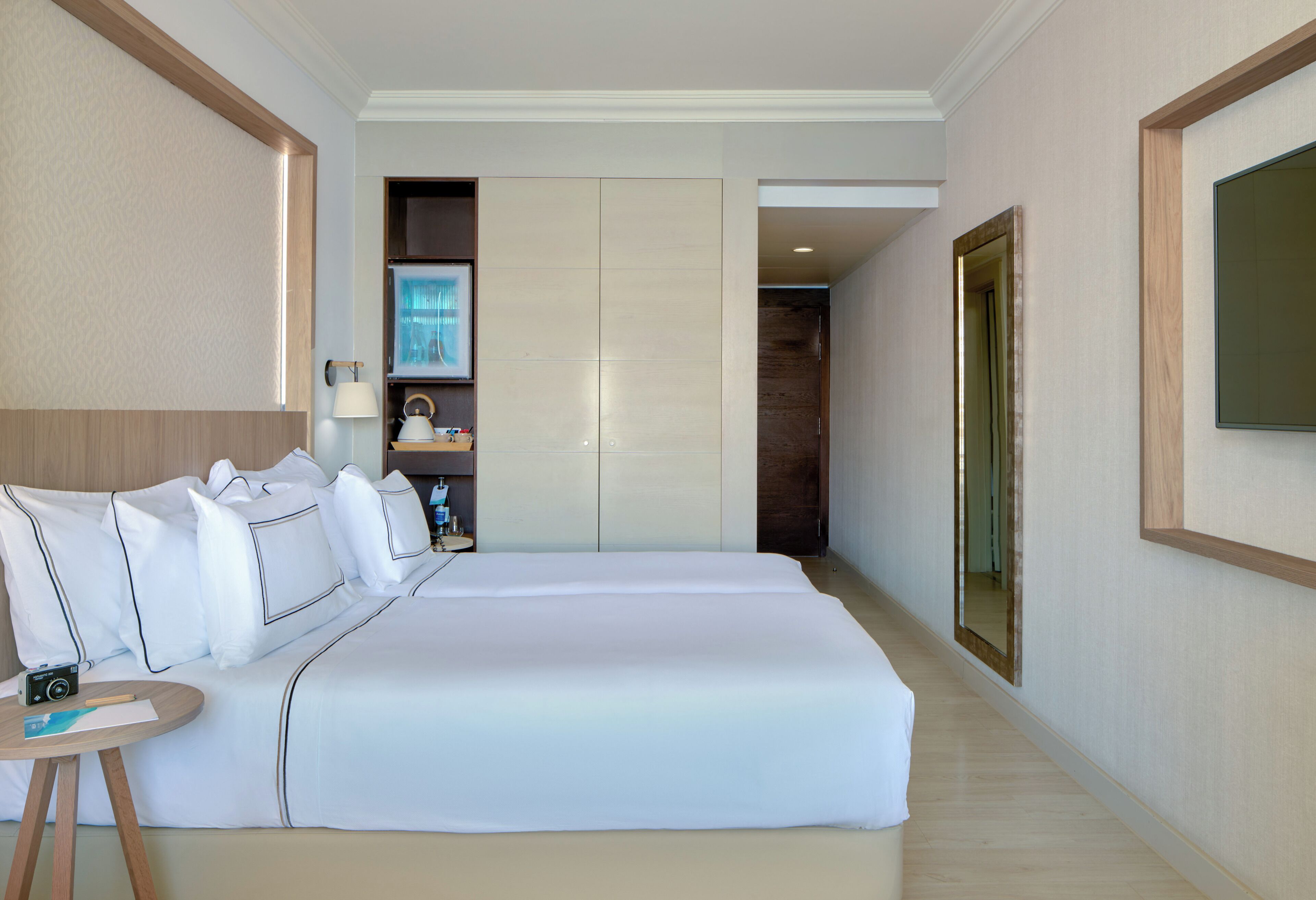 A hotel room with a large bed, a bedside table, a lamp, and a mirror.
