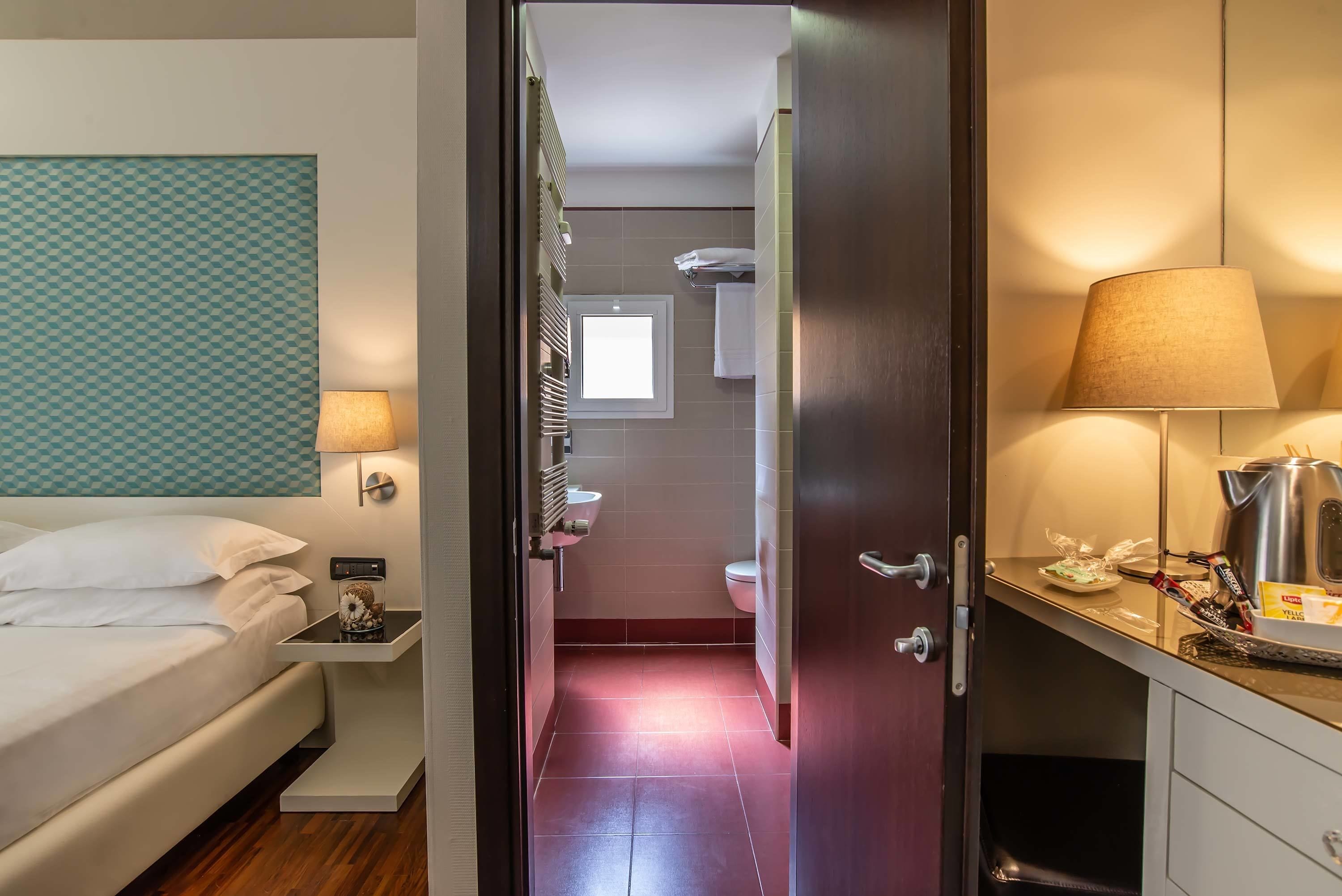 A hotel room with a bed, bedside table, lamp, and a view into the bathroom.