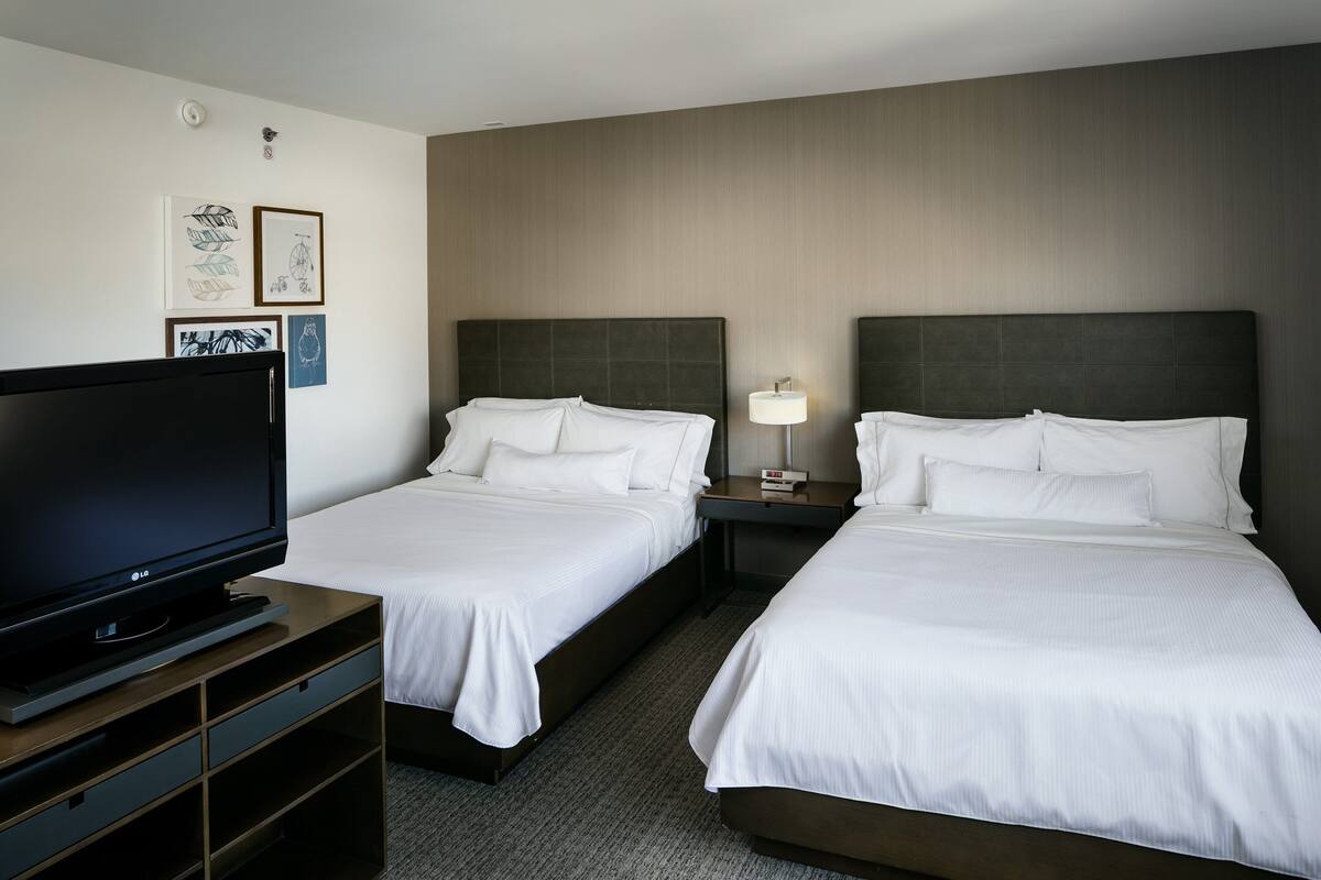 A hotel room with two beds, a TV, and artwork on the wall.