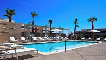 A pool area with white lounge chairs, palm trees, and a clear blue sky.
