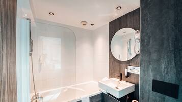 Un bagno moderno con cabina doccia in vetro, una vasca da bagno bianca, un lavabo con specchio e una parete scura con texture.