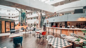 Un vaste espace intérieur aménagé avec de nombreux coins salon, un bar central et un escalier menant à un niveau supérieur.
