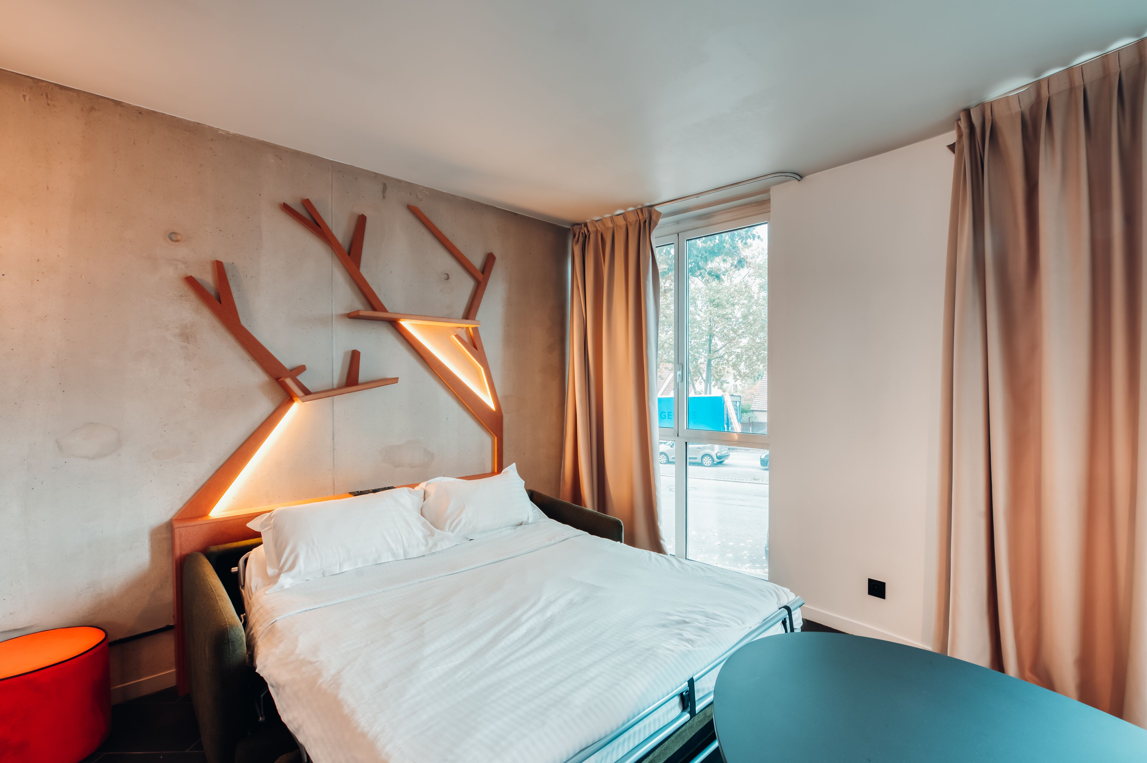 A hotel room with a bed, a table, a lamp, and a window with curtains.