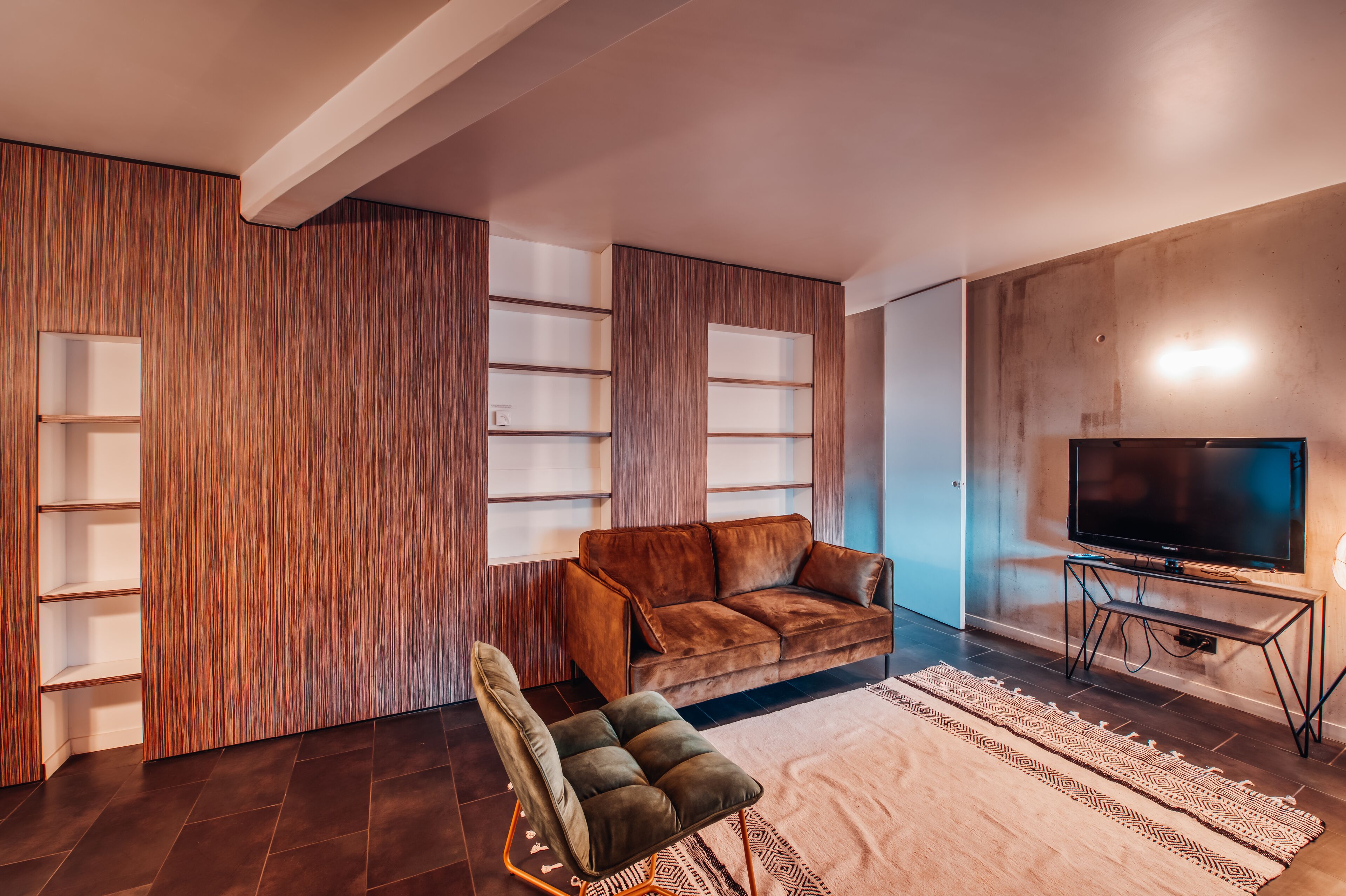 Een moderne woonkamer met een bruine leren bank, een zwarte televisie op een dressoir, en een kamerbreed tapijt met een patroon.