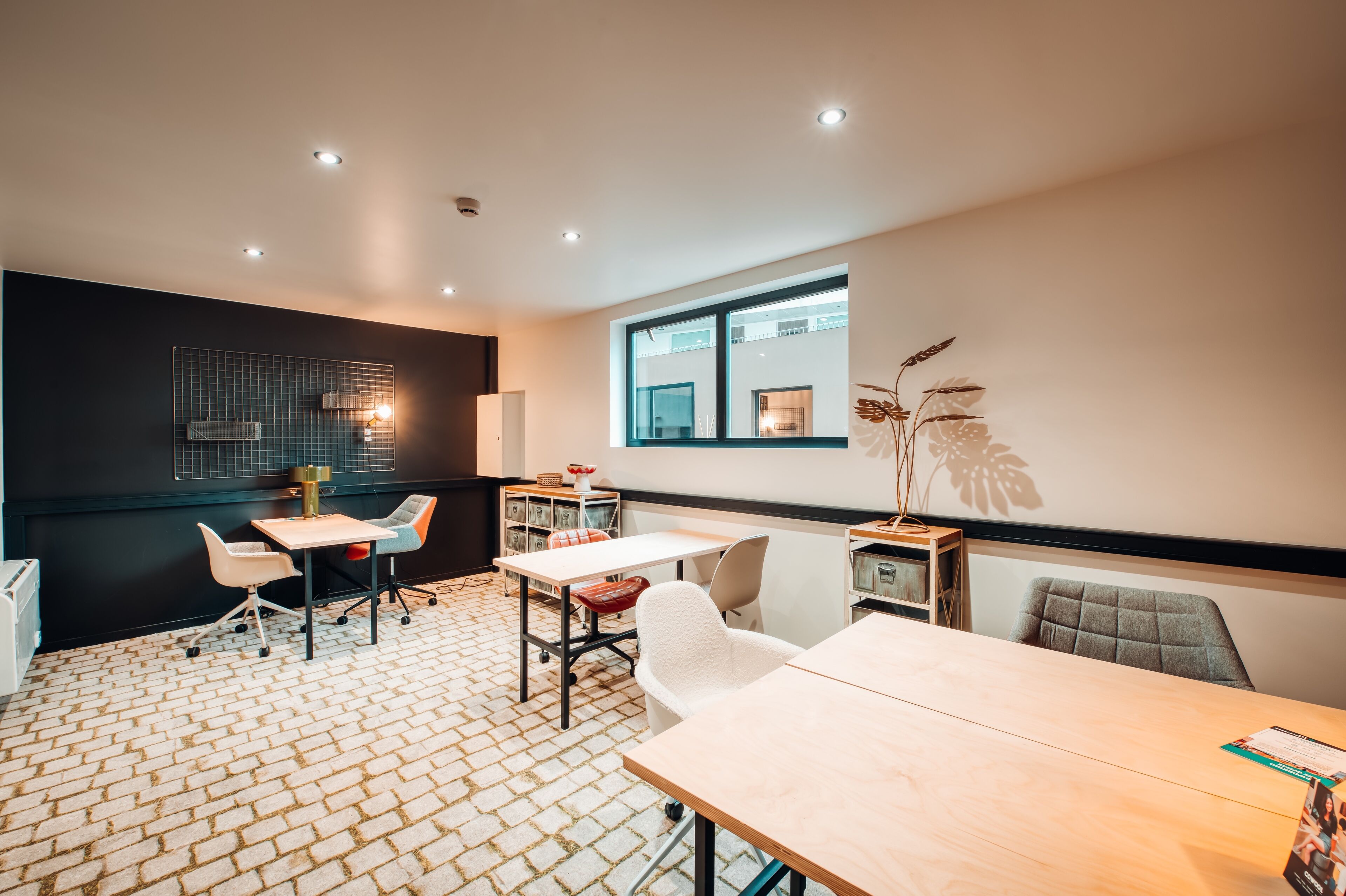 A modern meeting room with a brick-patterned floor, white and gray chairs, and a large window providing natural light.