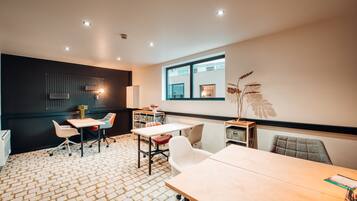 A modern meeting room with a brick-patterned floor, white and gray chairs, and a large window providing natural light.