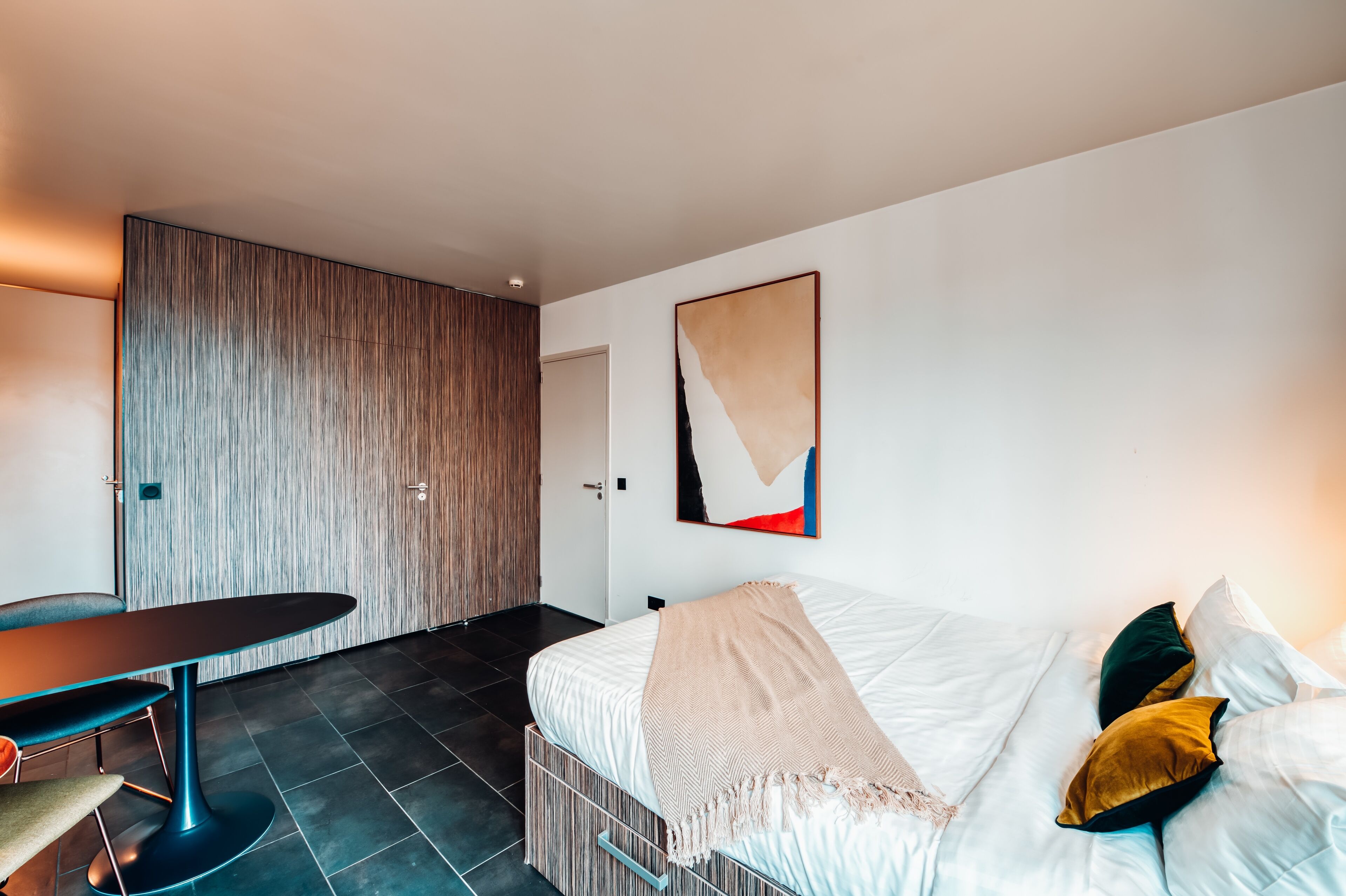 Een moderne hotelkamer met een bed, een bureau en een groot abstract schilderij aan de muur.