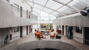 Un vaste atrium moderne doté d’un haut plafond, de grandes fenêtres et d’un espace de détente central avec des chaises orange.