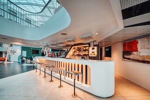 Zona de bar moderna con una barra curva, taburetes y un techo alto con tragaluces.
