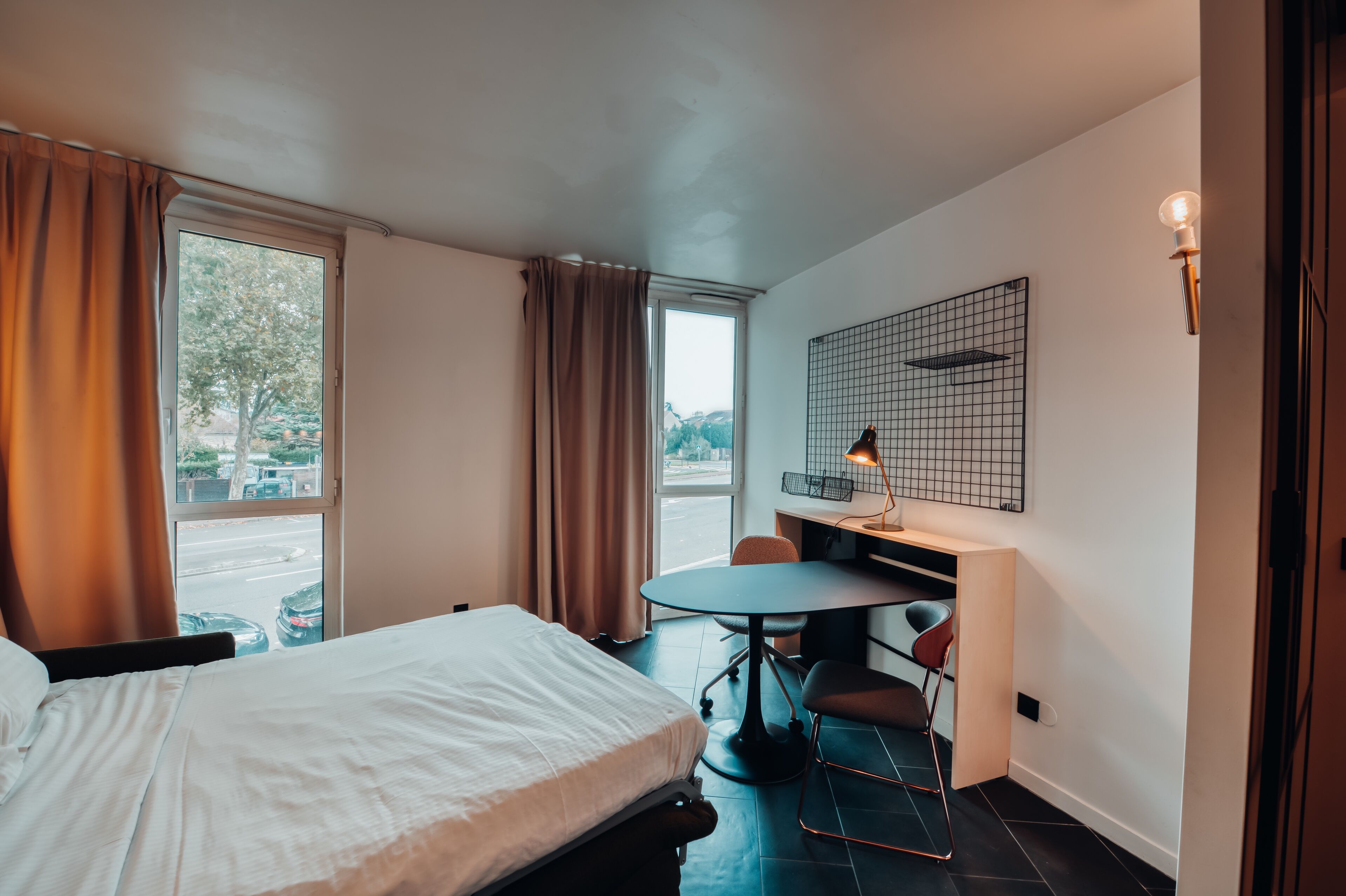 A hotel room with a bed, a desk, a chair, and a window with curtains.