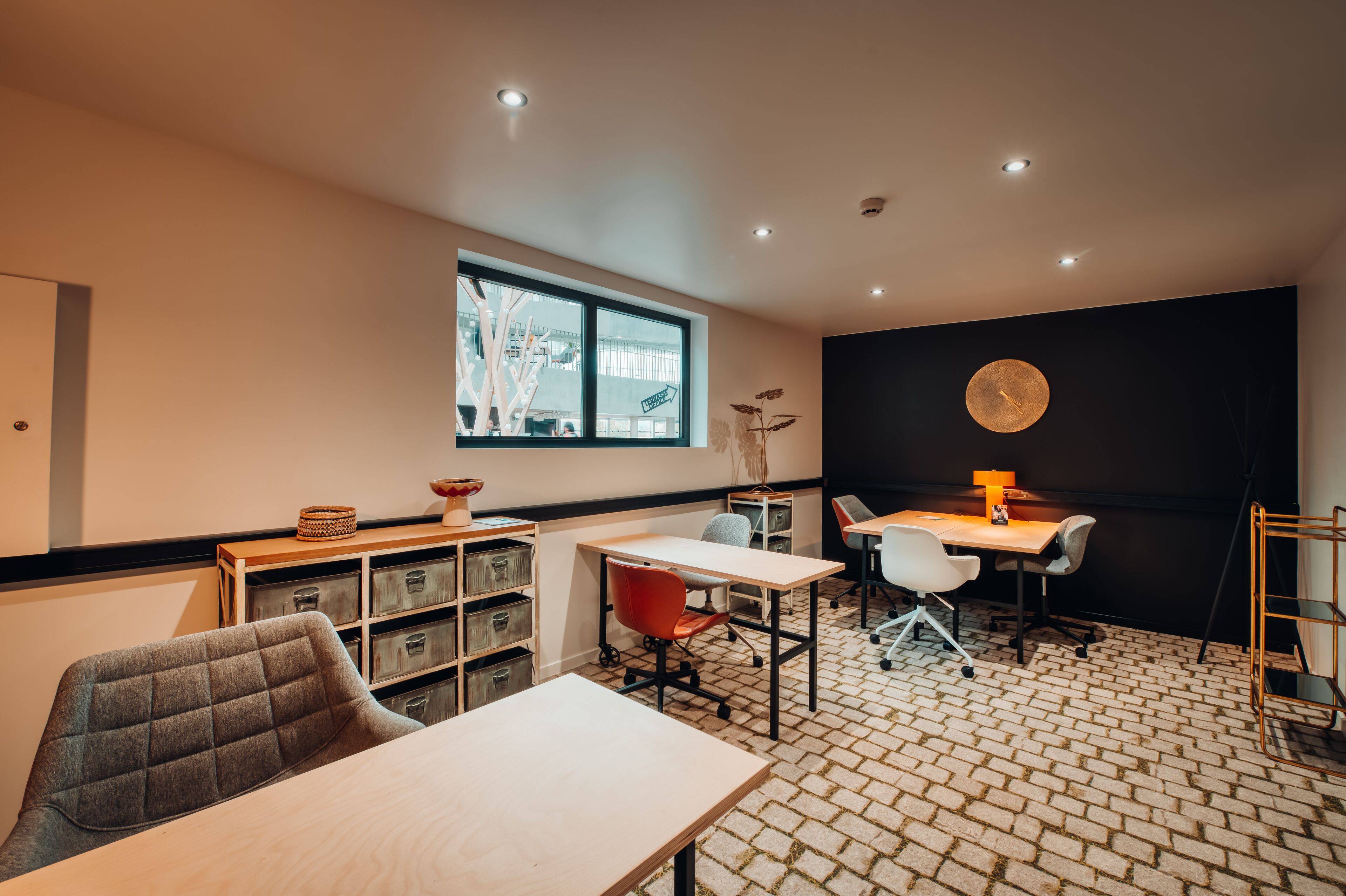 A modern meeting room with a large window, a round table, and a black accent wall.