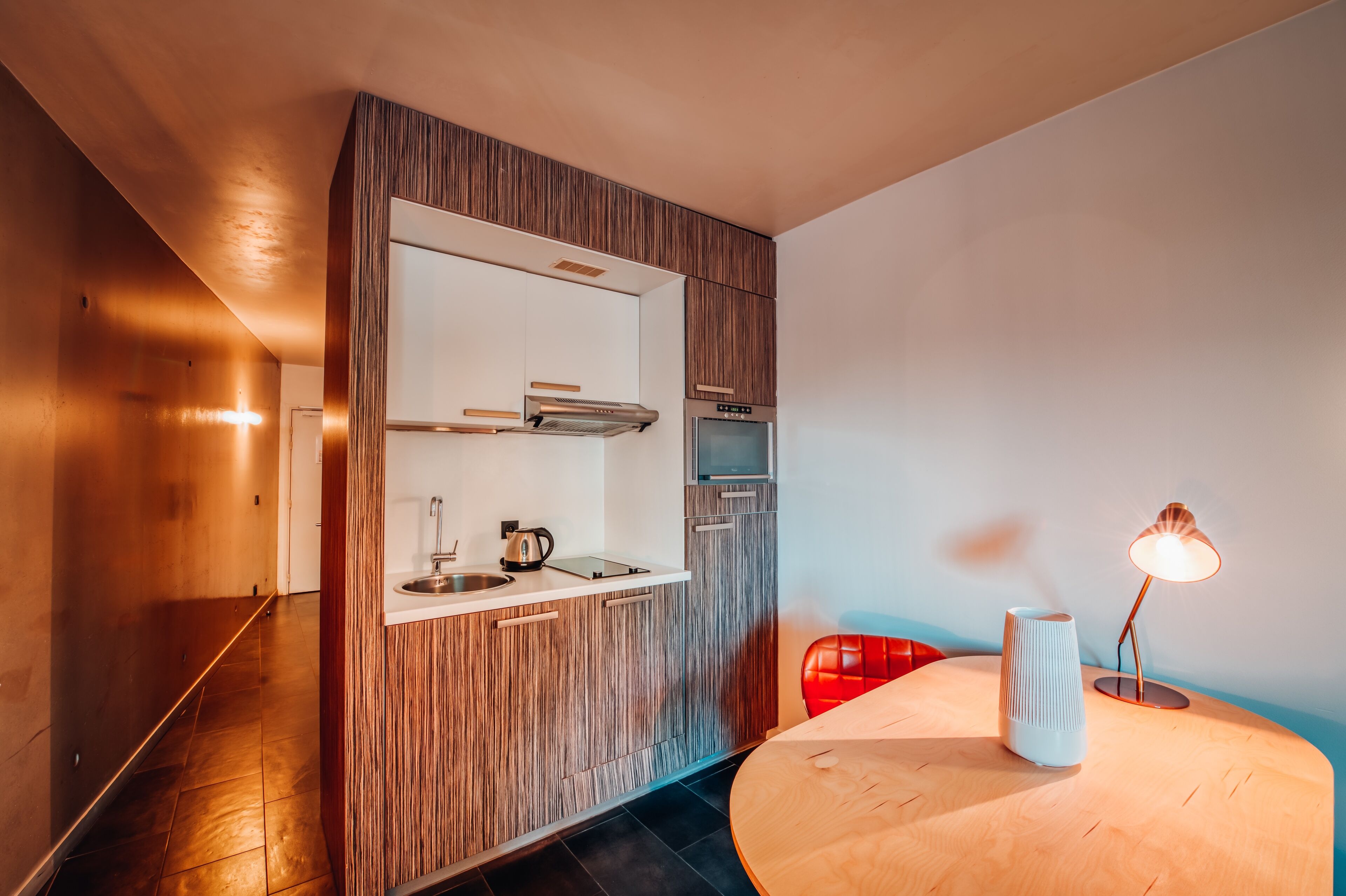 Una cocina moderna con armarios de madera, horno empotrado y una mesa redonda de madera con un jarrón blanco y una lámpara.