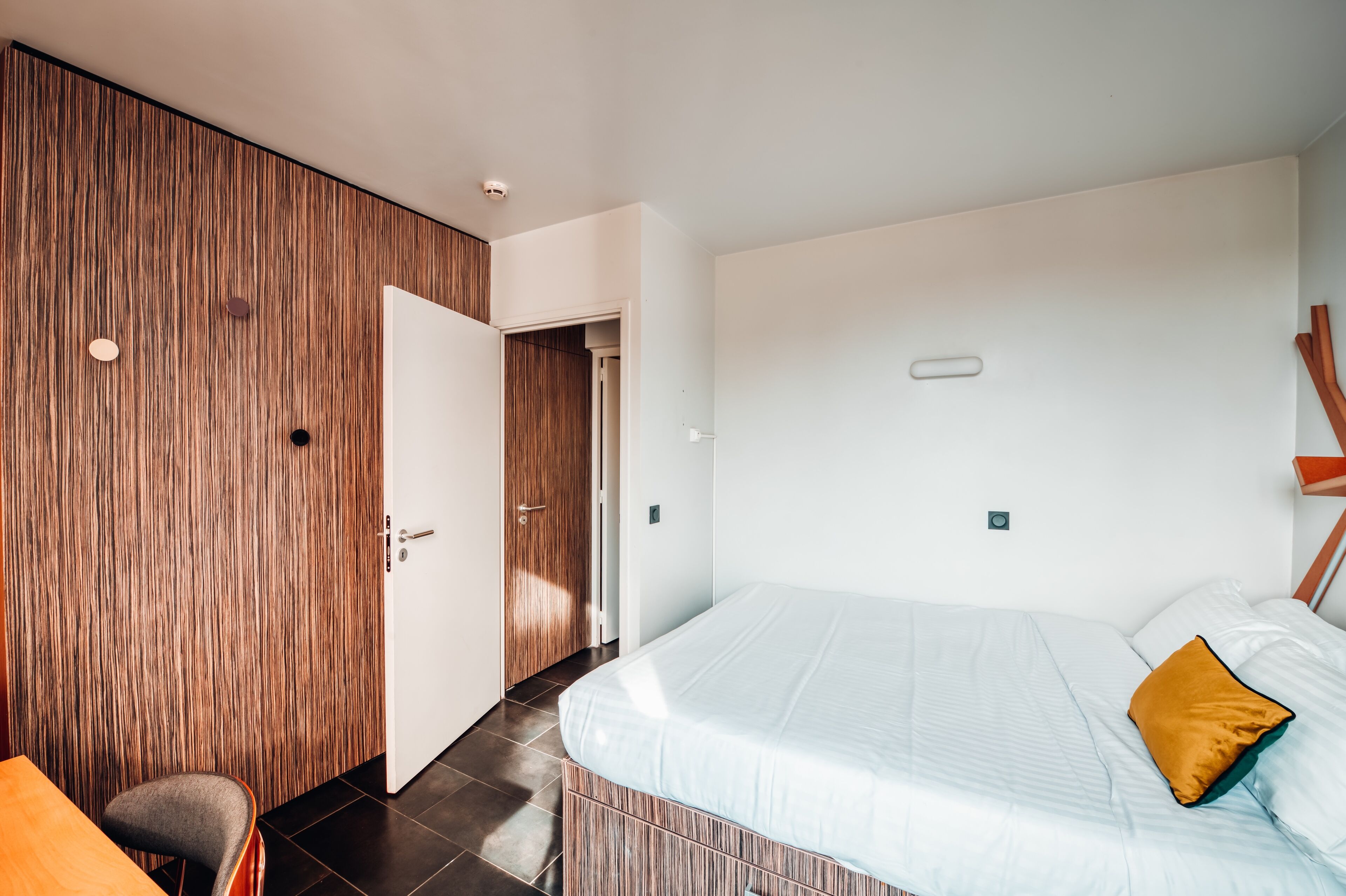 A modern bedroom with a large bed, a wooden wardrobe, and a small seating area.