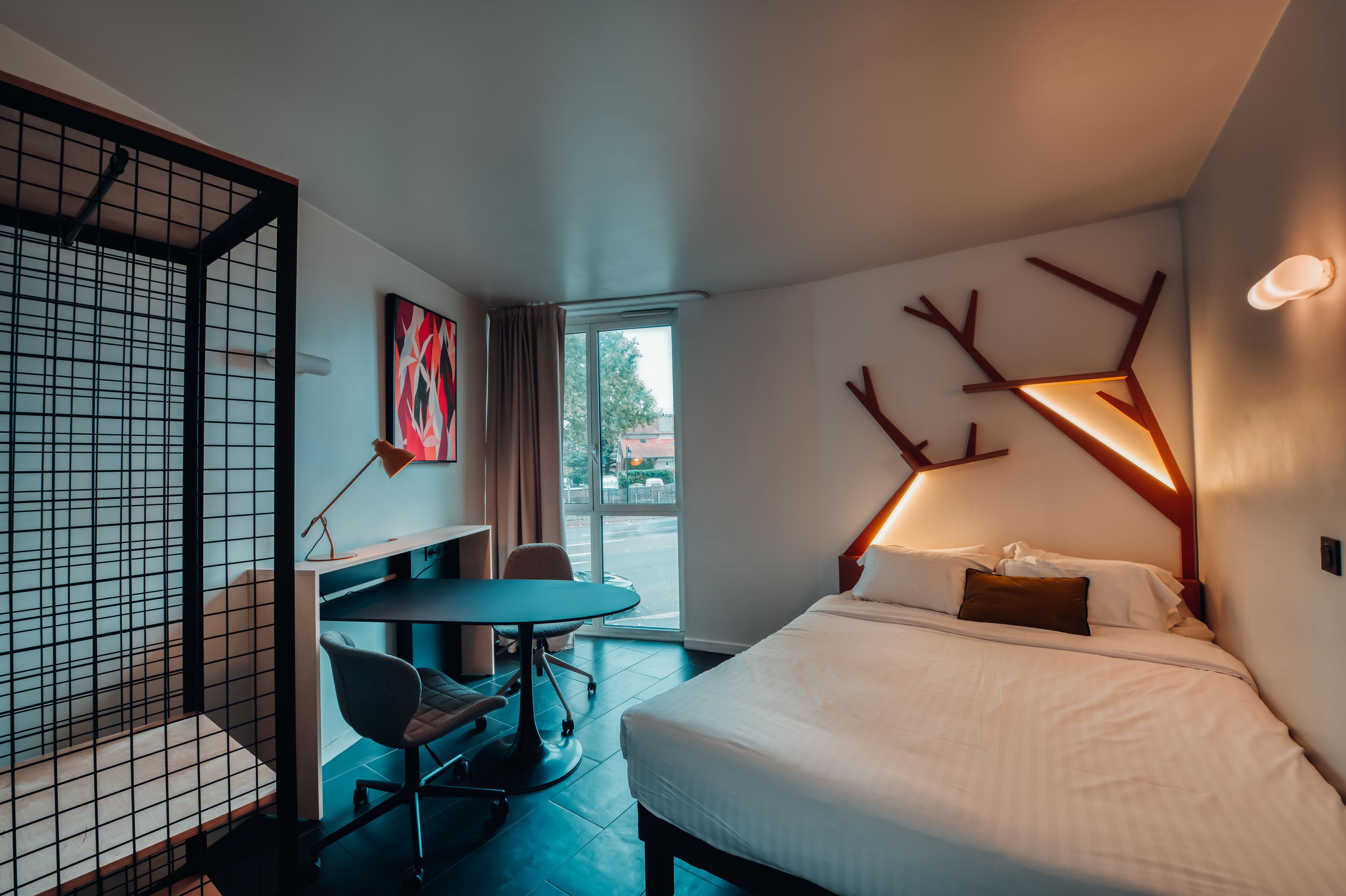 Une chambre d’hôtel moderne équipée d’un lit, d’un bureau, d’une chaise et d’une grande fenêtre.