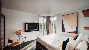 A modern hotel room with a large bed, a flat-screen TV mounted on the wall, a balcony with a view, and a minimalist decor style.