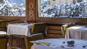 Um restaurante acolhedor com interiores de madeira e mesas preparadas para refeições, com vista para uma paisagem montanhosa coberta de neve.