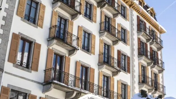 Um edifício com vários andares, varandas, persianas de madeira e entrada coberta de neve.