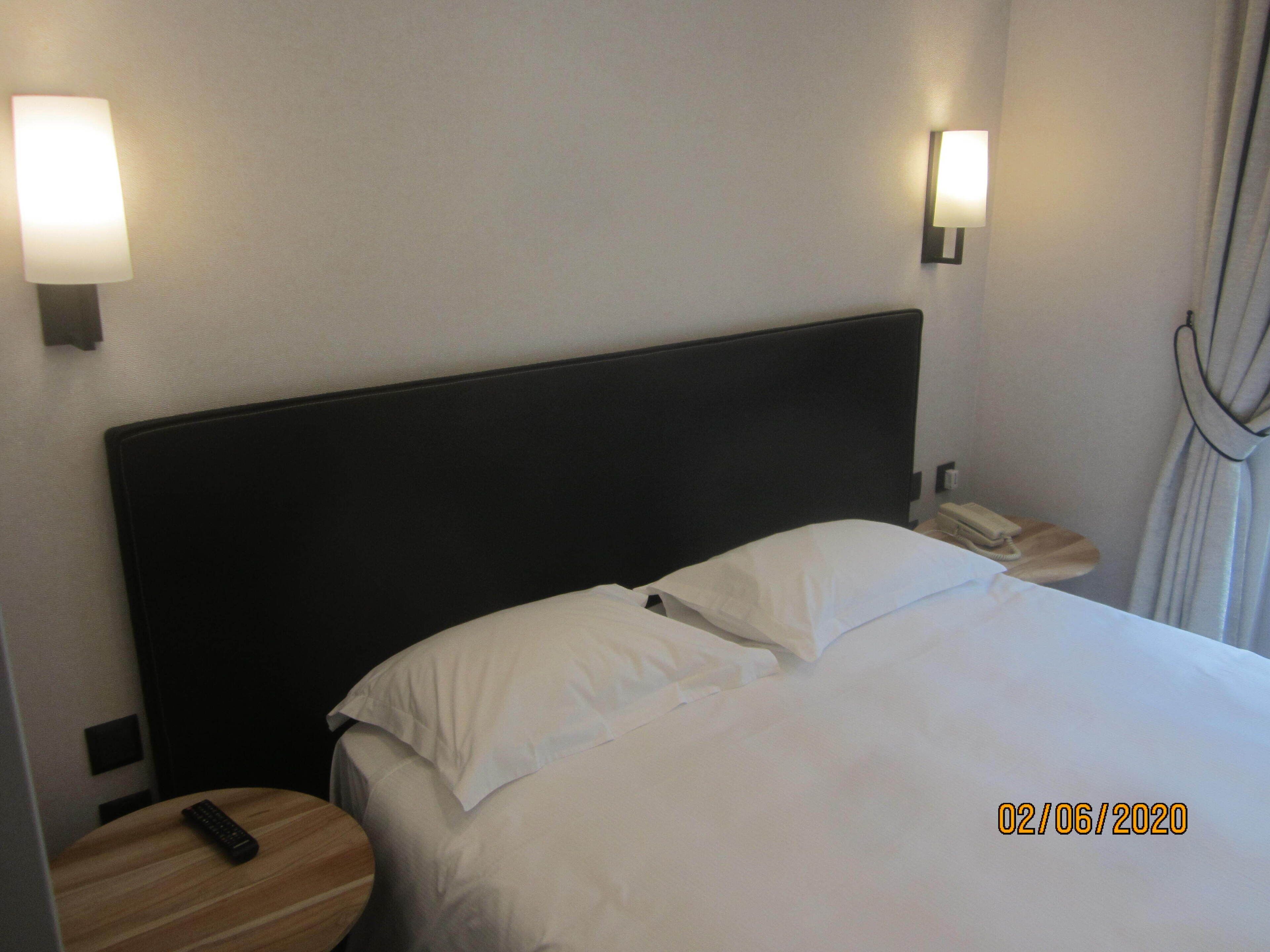 Une chambre d’hôtel avec un lit, deux tables de chevet, une télécommande et un téléphone posé sur l’une des tables.