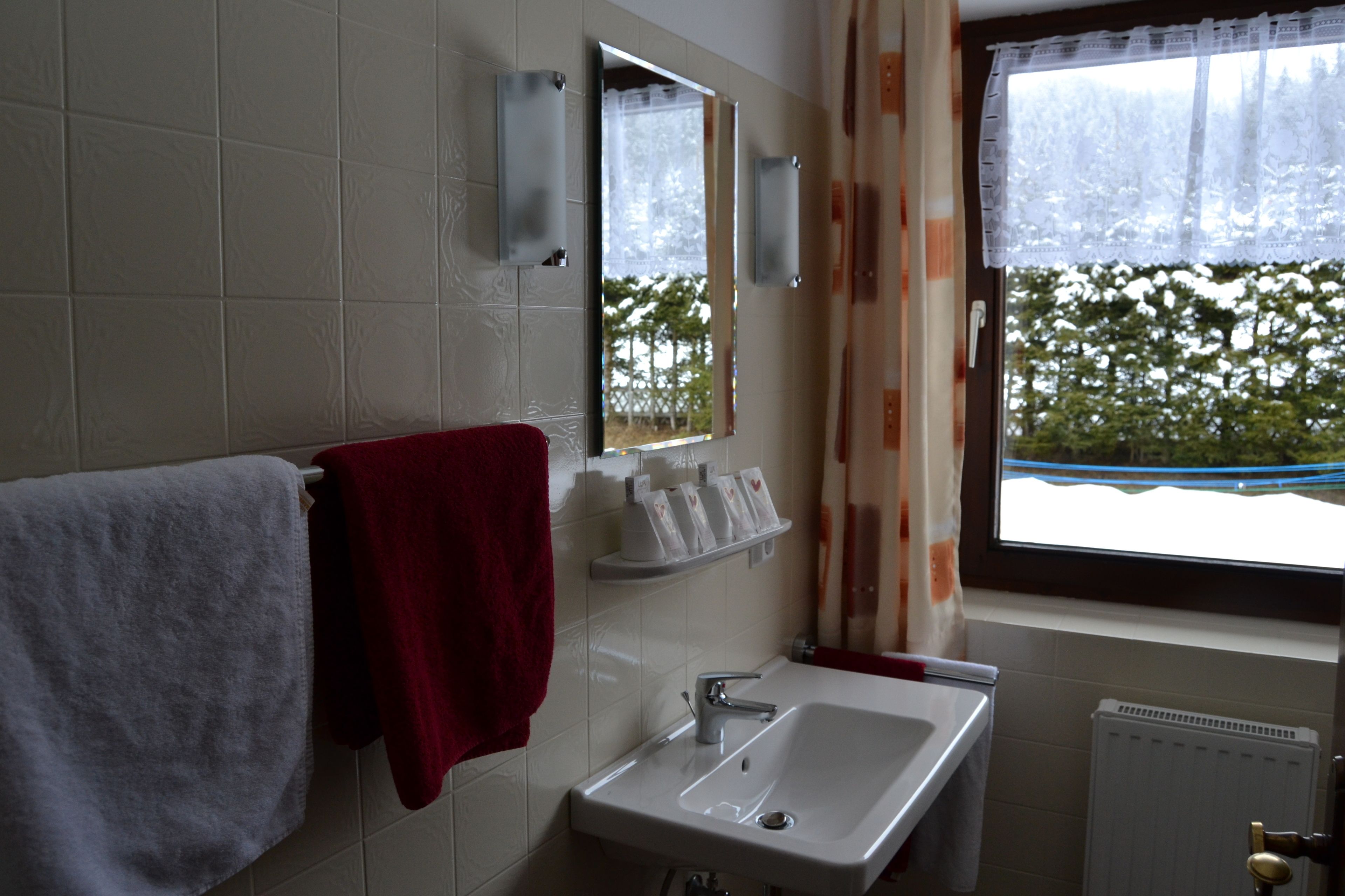 Un baño con un lavabo blanco, una toalla roja, un espejo y una ventana con vistas a árboles.