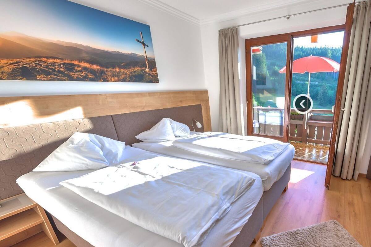 Een hotelkamer met een bed, een slaapbank, een schilderij en een balkon met een rode parasol.