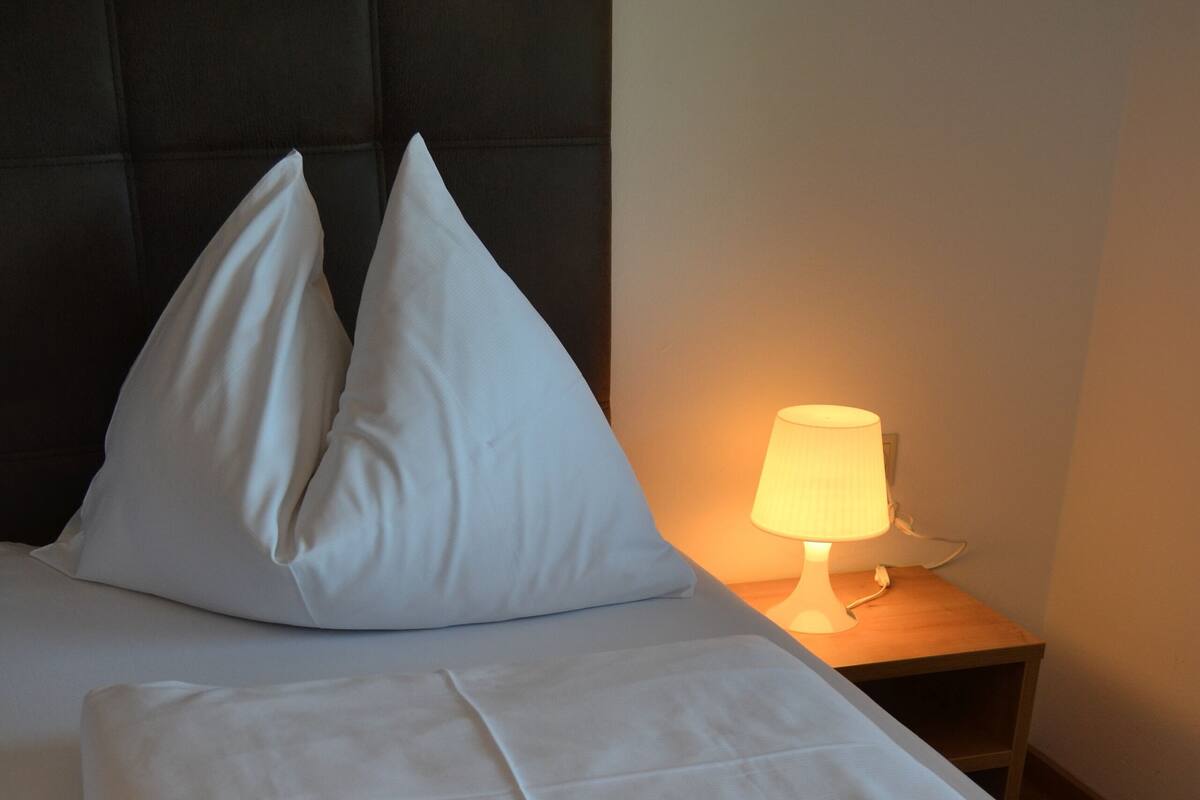 Een opgemaakt bed met kussens, een gevouwen handdoek en een bedlampje.