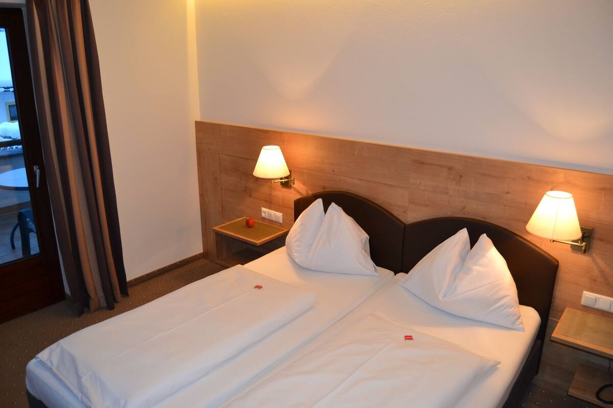 Een tweepersoonsbed met witte lakens, twee bedlampjes en een houten hoofdbord.
