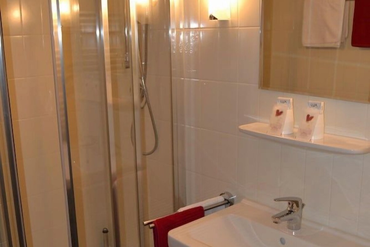 Een badkamer met een douche met glazen wand, een wastafel met spiegel erboven en een handdoekrek met een rode handdoek.