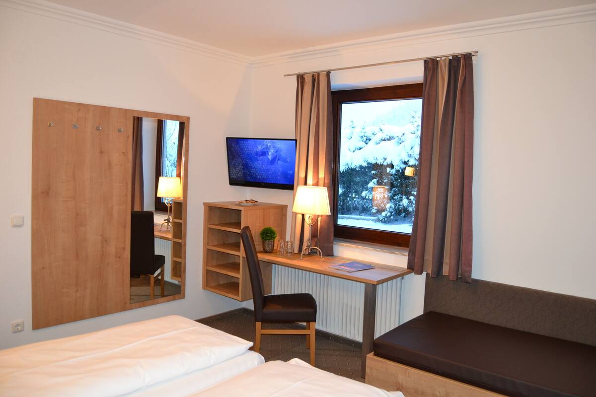 Een hotelkamer met een bed, een bureau met stoel, een televisie en een raam met gordijnen.